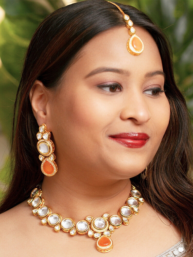 Close-up of a woman wearing an ornate traditional (Gold Polish) Peach Collar jewellery set and earrings and maangtikka with Kundan and American Diamonds. Woman wearing trending Kundan artificial jewelry for wedding season in India. Bride wearing a royal Kundan artificial necklace for wedding rituals.