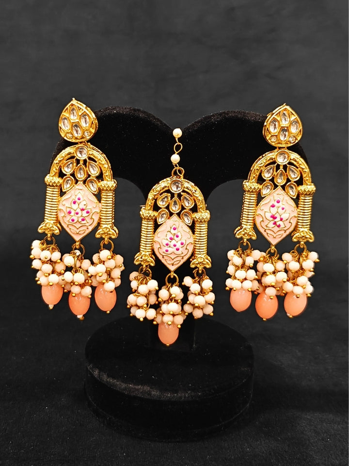Close-up of an ornate traditional (Gold Polish) Peach Choker jewellery set and earrings and maangtikka with Kundan, Meenakari, Crystal beads and Tumble beads. Close-up of intricate Kundan craftsmanship in artificial bridal jewelry. A traditional Kundan artificial necklace set for her wedding ceremony.
