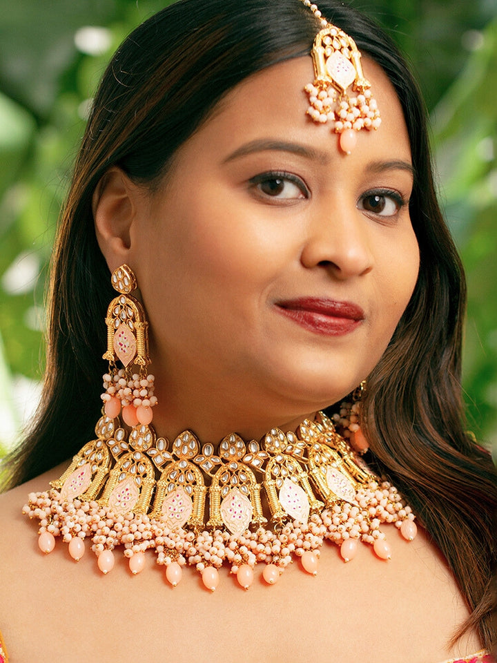 Close-up of a woman wearing an ornate traditional (Gold Polish) Peach Choker jewellery set and earrings and maangtikka with Kundan, Meenakari, Crystal beads and Tumble beads. Close-up of intricate Kundan craftsmanship in artificial bridal jewelry. Bride wearing a traditional Kundan artificial necklace set for her wedding ceremony.
