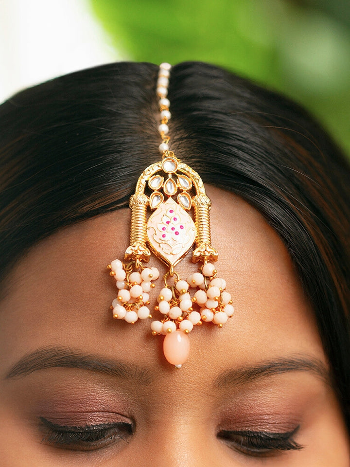 Close-up of a woman wearing an ornate traditional (Gold Polish) Peach Choker jewellery set and earrings and maangtikka with Kundan, Meenakari, Crystal beads and Tumble beads. Close-up of intricate Kundan craftsmanship in artificial bridal jewelry. Bride wearing a traditional Kundan artificial necklace set for her wedding ceremony.