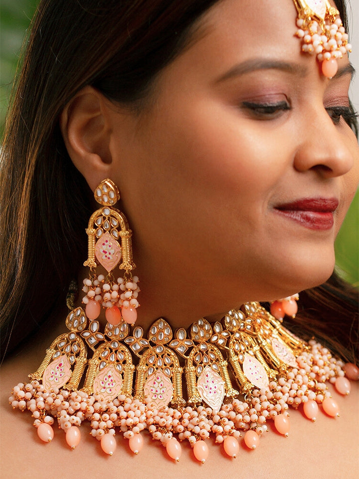Close-up of a woman wearing an ornate traditional (Gold Polish) Peach Choker jewellery set and earrings and maangtikka with Kundan, Meenakari, Crystal beads and Tumble beads. Close-up of intricate Kundan craftsmanship in artificial bridal jewelry. Bride wearing a traditional Kundan artificial necklace set for her wedding ceremony.