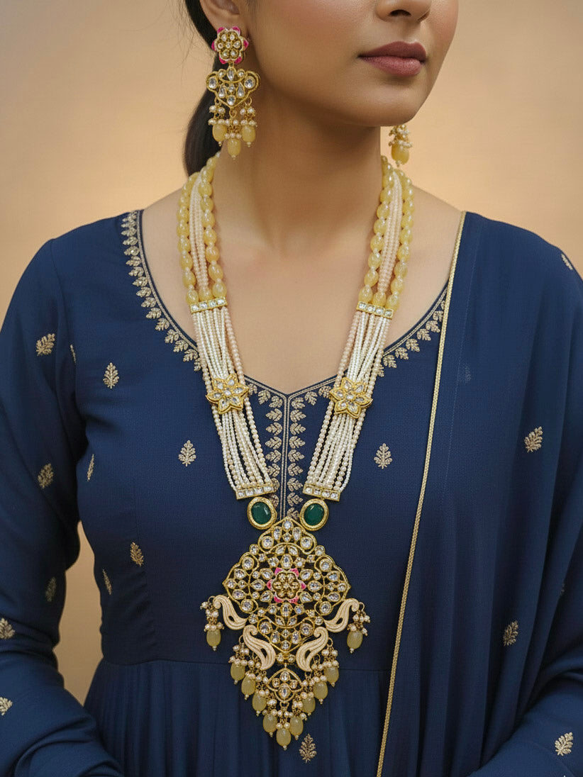Close-up of a woman wearing an ornate traditional Peach Rajwadi gold Long jewellery set and earrings with Kundan, Meenakari work, crystal beads, pearls, American Diamonds, pearls, Tumble stones and Colored Stones. Woman wearing a bridal Rajwadi necklace for a reception function. Close-up of a handcrafted Rajwadi artificial jewelry set for bridal wear.