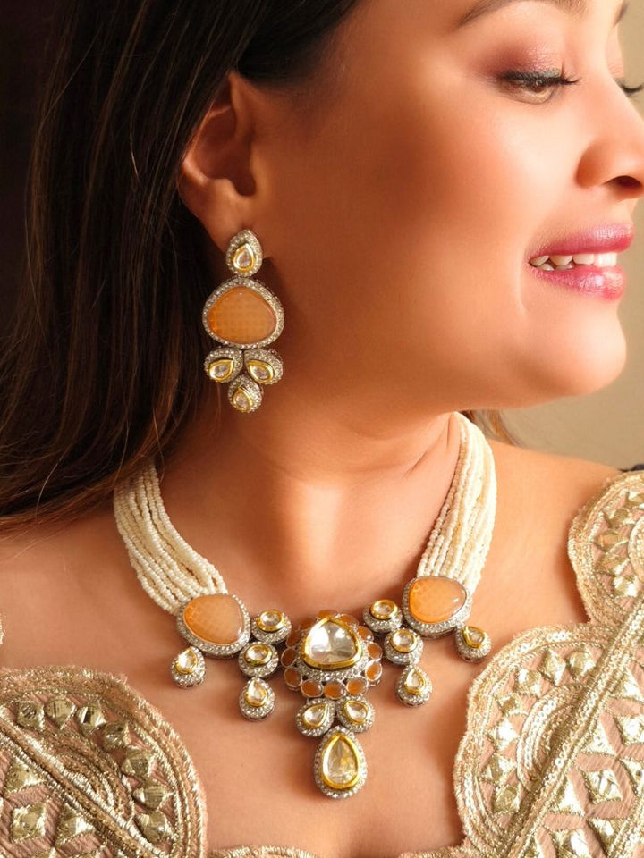 A woman in a gold embroidered outfit smiles, showcasing the Peacoski Peach Tamanna Necklace Set and matching earrings. Her soft makeup highlights the elegance of this statement jewelry ensemble.