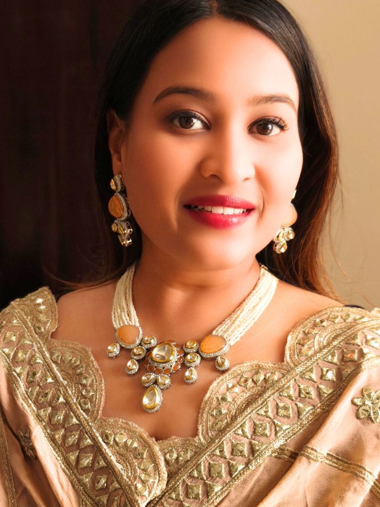 A woman in a gold embroidered outfit smiles, showcasing the Peacoski Peach Tamanna Necklace Set and matching earrings. Her soft makeup highlights the elegance of this statement jewelry ensemble.