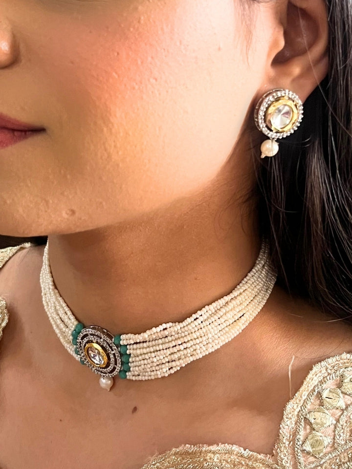 A woman wears the Pearl Teel Renu Necklace Set, featuring a multi-strand white pearl choker with Kundan and Teel accents, a central jeweled pendant, and matching round earrings adorned with dangling pearls. Kundan choker necklace accentuates her look.