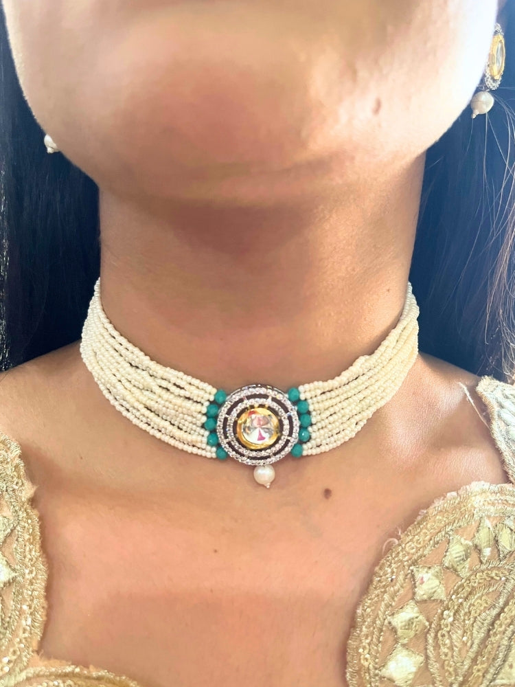 A woman wears the Pearl Teel Renu Necklace Set, featuring a multi-strand white pearl choker with Kundan and Teel accents, a central jeweled pendant, and matching round earrings adorned with dangling pearls. Kundan choker necklace accentuates her look.