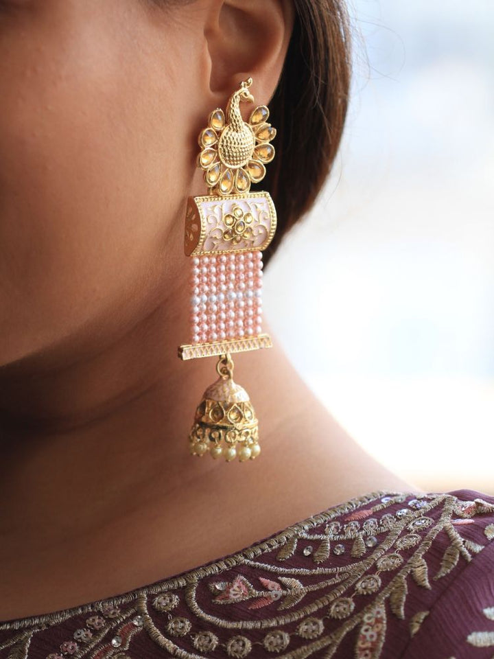Close-up of a womans ear wearing Pink Akriti Long Jhumki Earrings, featuring an ornate peacock design on top, with pink bead strands, and a dangling jhumka—an ethnic piece beautifully complementing her maroon embroidered wedding attire.