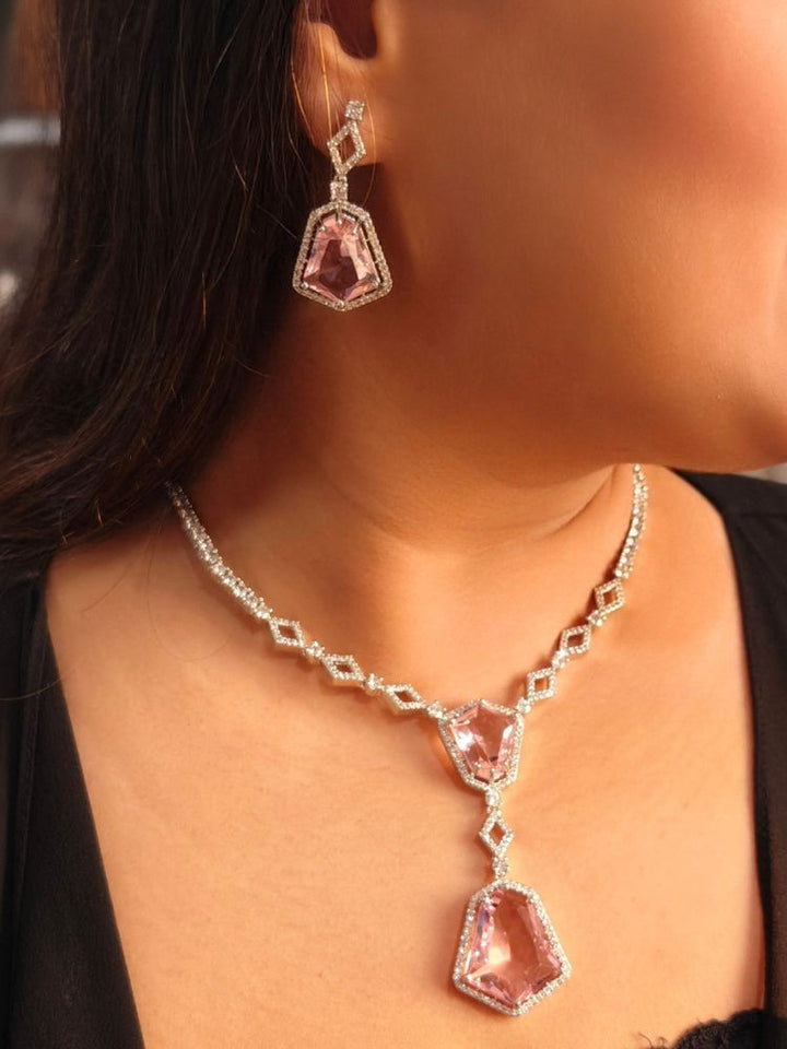 A woman showcases the Angela Pink Necklace Set, featuring matching jewelry with bold Pink stones and sparkling American Diamonds on both drop earrings and a geometric pendant necklace for a striking look.
