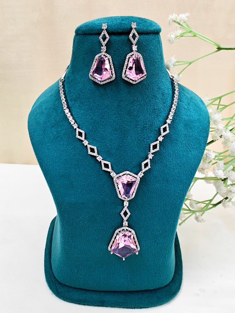 Angela Pink Necklace Set, featuring matching jewelry with bold Pink stones and sparkling American Diamonds on both drop earrings and a geometric pendant necklace for a striking look. Set on a blue dummy. 