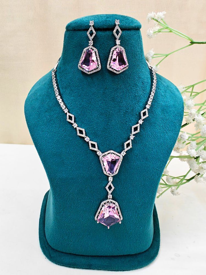 Angela Pink Necklace Set, featuring matching jewelry with bold Pink stones and sparkling American Diamonds on both drop earrings and a geometric pendant necklace for a striking look. Set on a blue dummy. 