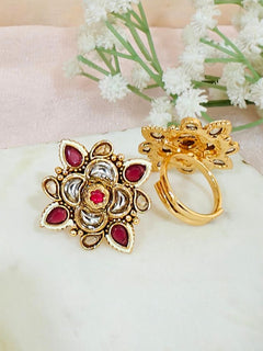 The Pink Chhavi Ring features ornate gold brass ring with floral designs and Pink, white, and red colored stones. Adjustable and elegant, it’s shown on marble with White flowers in the background—perfect for elevating any look.