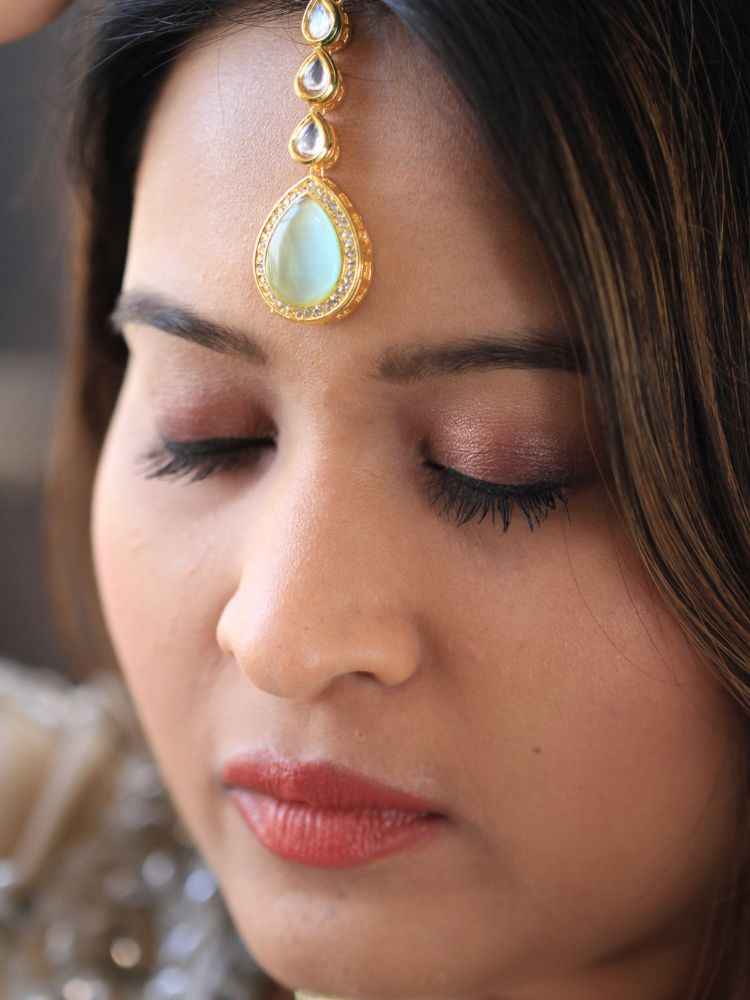 Close-up of a woman wearing an ornate traditional (Gold Polish) Pink & Green Collar jewellery set and earrings and maangtikka with Kundan and American Diamonds. Woman wearing trending Kundan artificial jewelry for wedding season in India. Bride wearing a royal Kundan artificial necklace for wedding rituals.