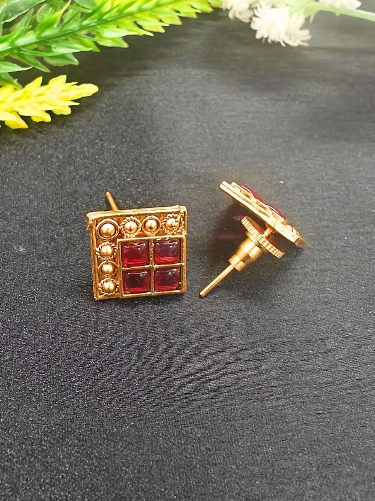 The Pink Vanita Earrings are square gold earrings with four red gemstones and gold bead detailing, shown on a black surface with yellow and white flowers—ideal for adding traditional flair to your Kurti ensemble.