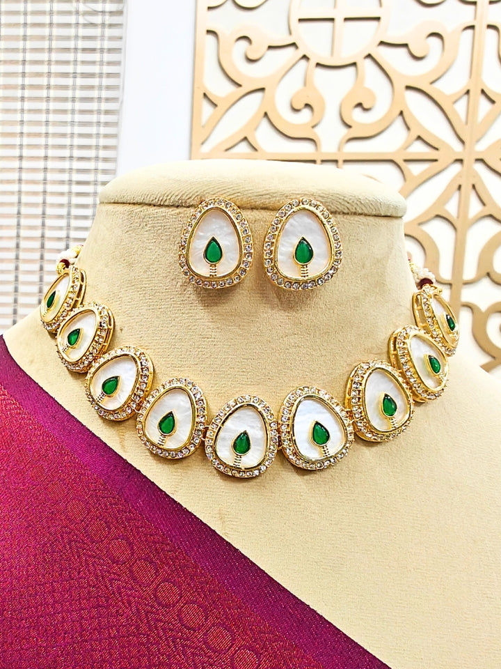 The Pragati Green Necklace Set features white necklace and matching earrings with white oval stones, surrounded by american diamonds, and teardrop-shaped multicolored gems in the center of each oval—perfect Wedding Ceremony Jewelry, shown on a mannequin bust.