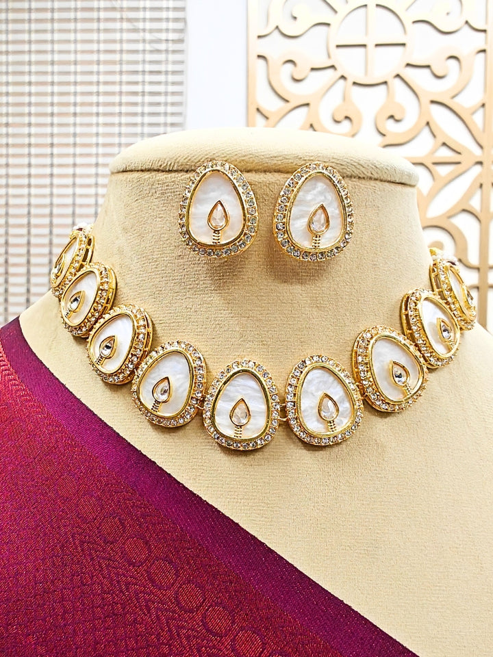 The Pragati White Necklace Set features white necklace and matching earrings with white oval stones, surrounded by american diamonds, and teardrop-shaped multicolored gems in the center of each oval—perfect Wedding Ceremony Jewelry, shown on a mannequin bust.