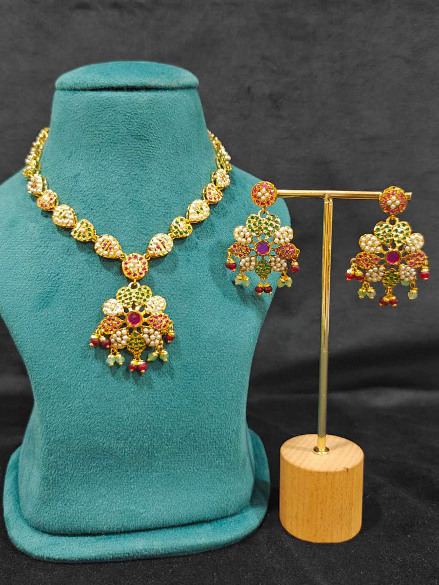 Close-up of an ornate traditional Collar Ruby Pink & Green jadau gold jewellery set and jadau earrings with beads and Color Stone. Close-up of intricate Jadau detailing in artificial jewelry. Festive celebration look featuring a Jadau artificial necklace.