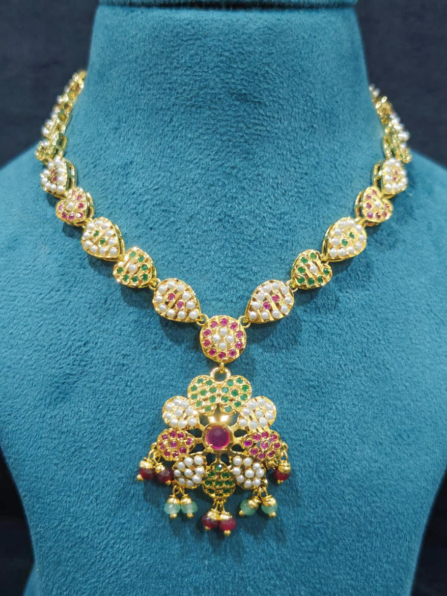 Close-up of an ornate traditional Collar Ruby Pink & Green jadau gold jewellery set and jadau earrings with beads and Color Stone. Close-up of intricate Jadau detailing in artificial jewelry. Festive celebration look featuring a Jadau artificial necklace.