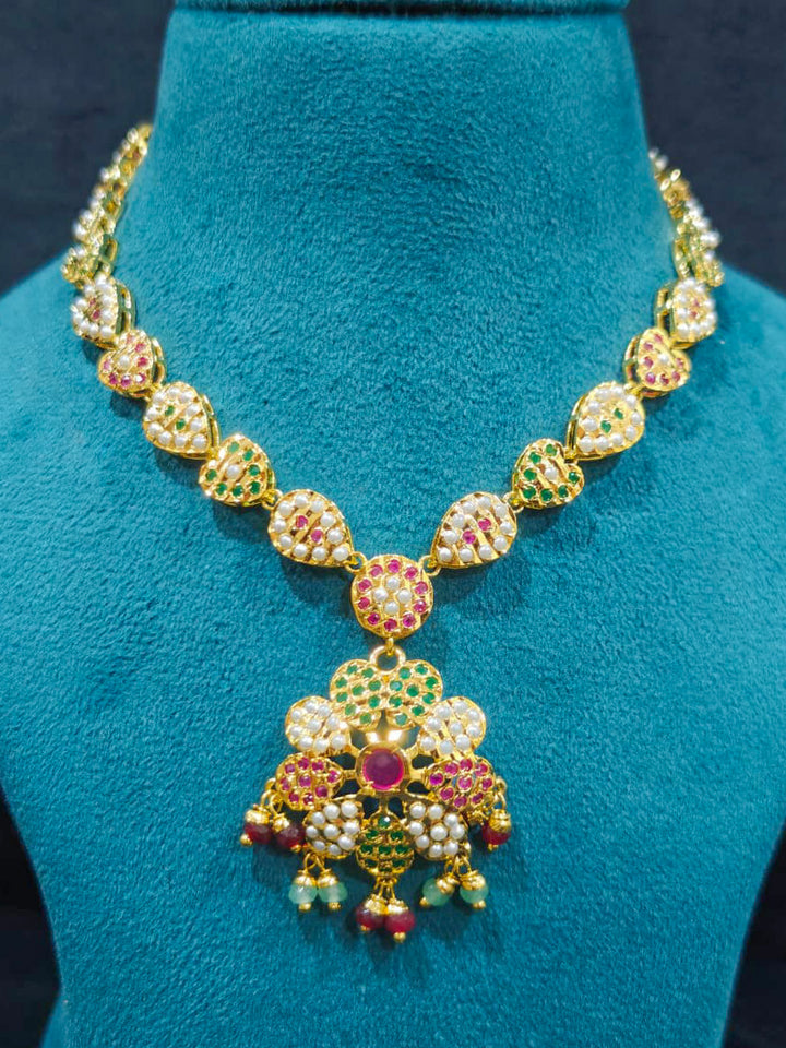 Close-up of an ornate traditional Collar Ruby Pink & Green jadau gold jewellery set and jadau earrings with beads and Color Stone. Close-up of intricate Jadau detailing in artificial jewelry. Festive celebration look featuring a Jadau artificial necklace.