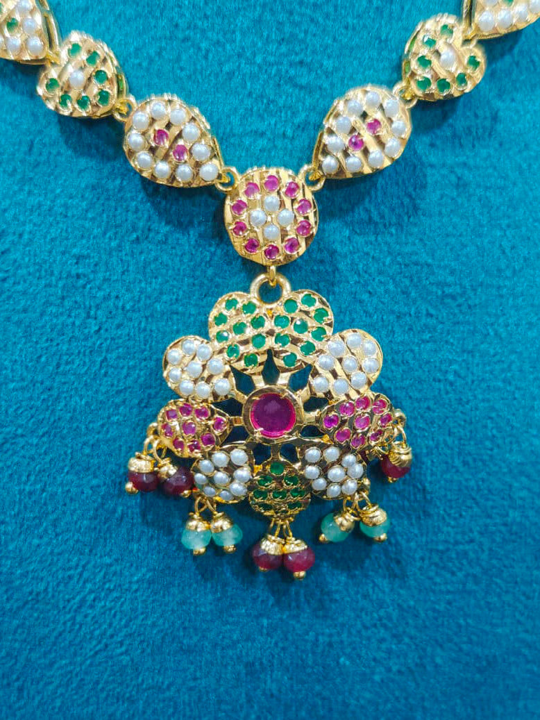 Close-up of an ornate traditional Collar Ruby Pink & Green jadau gold jewellery set and jadau earrings with beads and Color Stone. Close-up of intricate Jadau detailing in artificial jewelry. Festive celebration look featuring a Jadau artificial necklace.