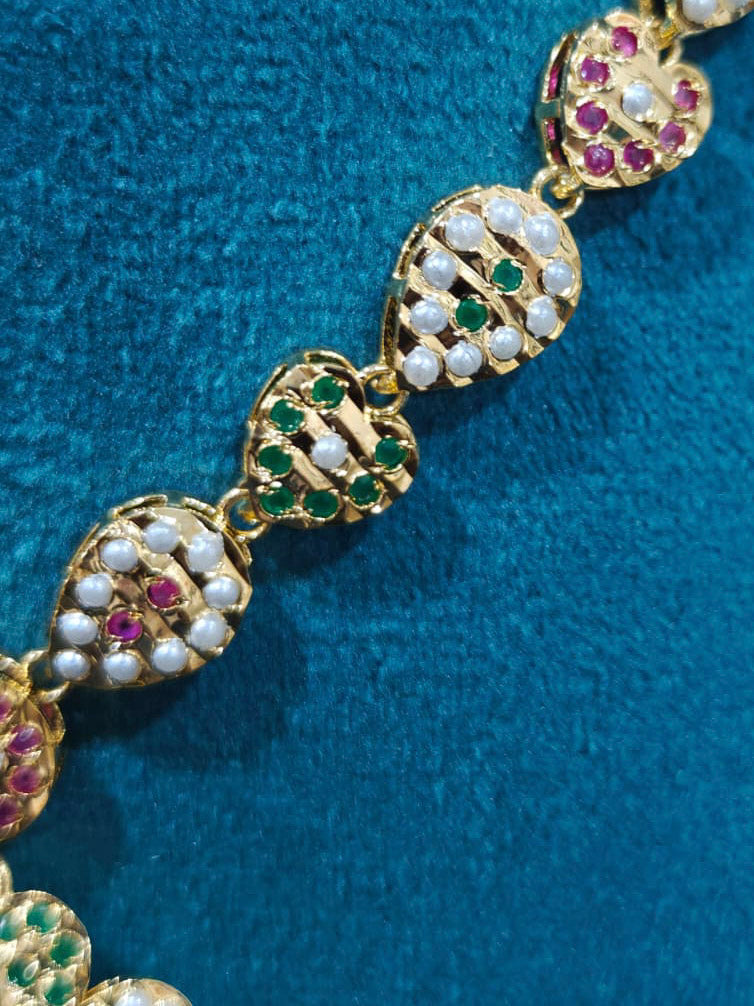 Close-up of an ornate traditional Collar Ruby Pink & Green jadau gold jewellery set and jadau earrings with beads and Color Stone. Close-up of intricate Jadau detailing in artificial jewelry. Festive celebration look featuring a Jadau artificial necklace.