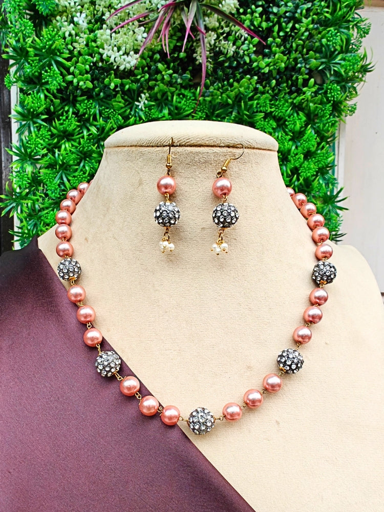 The Pranshi Necklace Set, featuring a pink pearl and silver bead necklace with matching dangle earrings, is displayed on a mannequin against lush green leaves—perfect for complementing a wedding ceremony dress.