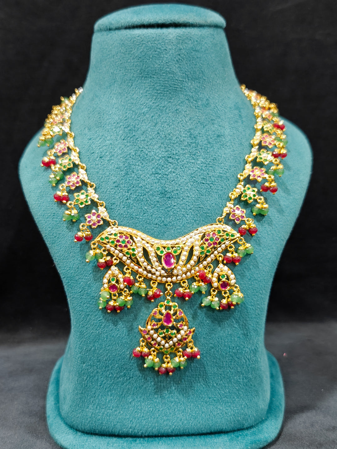Close-up of a gold Indian traditional jadau jewellery with crystal beads and ruby pink and green jadau stones and matching jadau earrings. Festive celebration look featuring a Jadau artificial necklace. Festive saree look completed with a handcrafted Jadau necklace.
