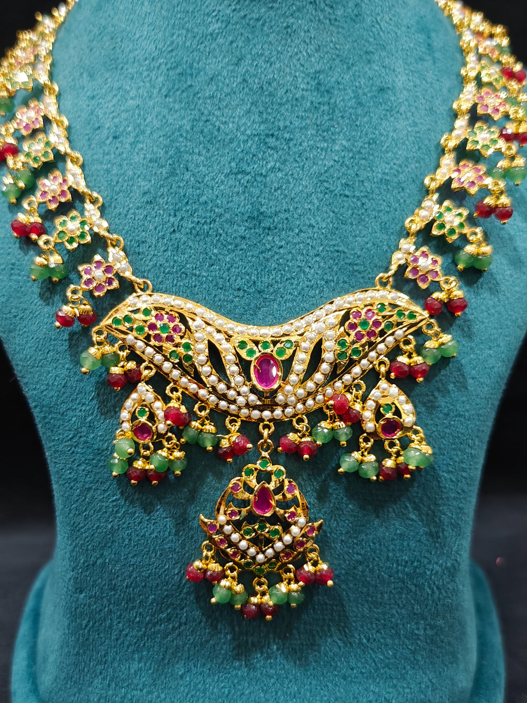 Close-up of a gold Indian traditional jadau jewellery with crystal beads and ruby pink and green jadau stones and matching jadau earrings. Mehendi function outfit styled with a lightweight Jadau necklace.

