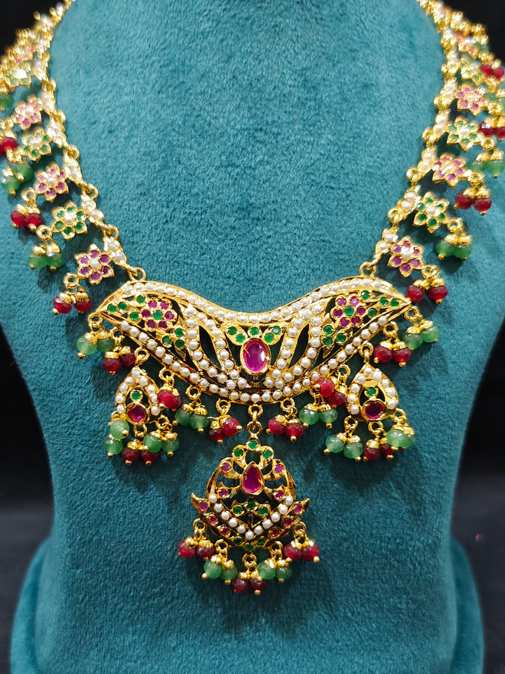 Close-up of a gold Indian traditional jadau jewellery with crystal beads and ruby pink and green jadau stones and matching jadau earrings. Mehendi function outfit styled with a lightweight Jadau necklace.
