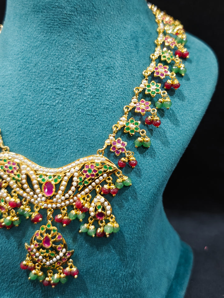 Close-up of a gold Indian traditional jadau jewellery with crystal beads and ruby pink and green jadau stones and matching jadau earrings. Festive celebration look featuring a Jadau artificial necklace. Close-up of intricate Jadau detailing.