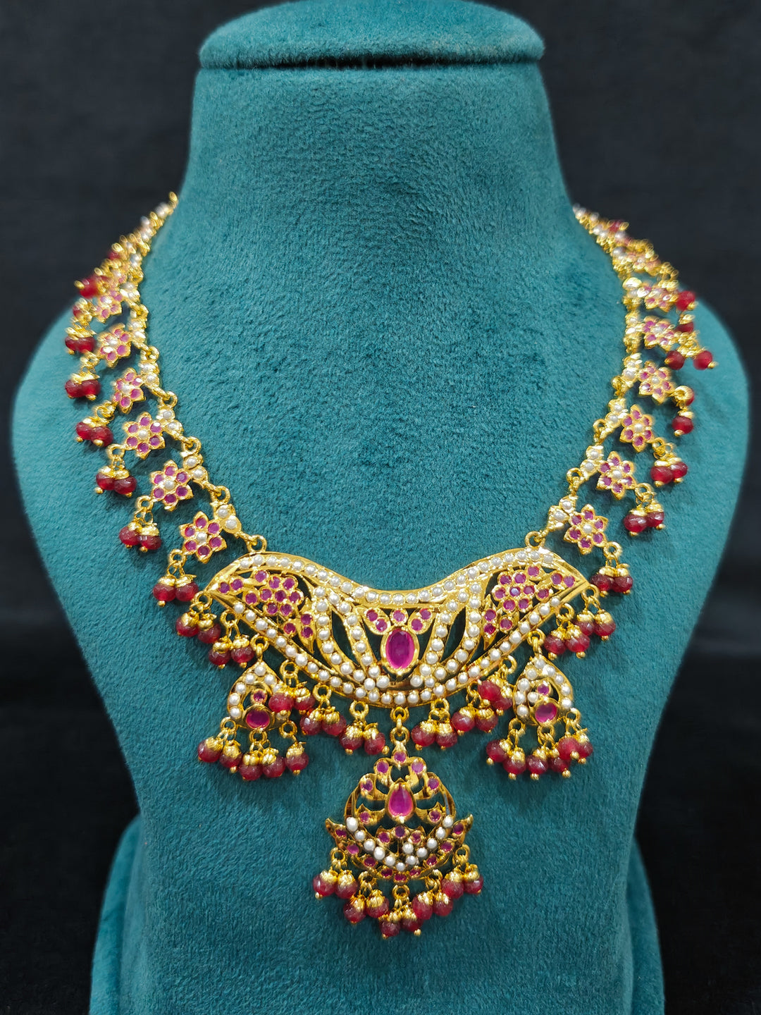 Close-up of a gold Indian traditional jadau jewellery with crystals beads and ruby pink jadau stones. This authentic jadau jewelry set can we worn as jadau necklace set for weddings. Festive celebration look featuring a Jadau artificial necklace.