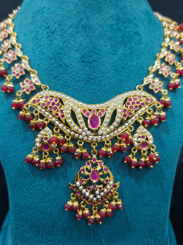 Close-up of a gold Indian traditional jadau jewellery with crystals beads and ruby pink jadau stones. This authentic jadau jewelry set can we worn as jadau necklace set for weddings. Festive celebration look featuring a Jadau artificial necklace.