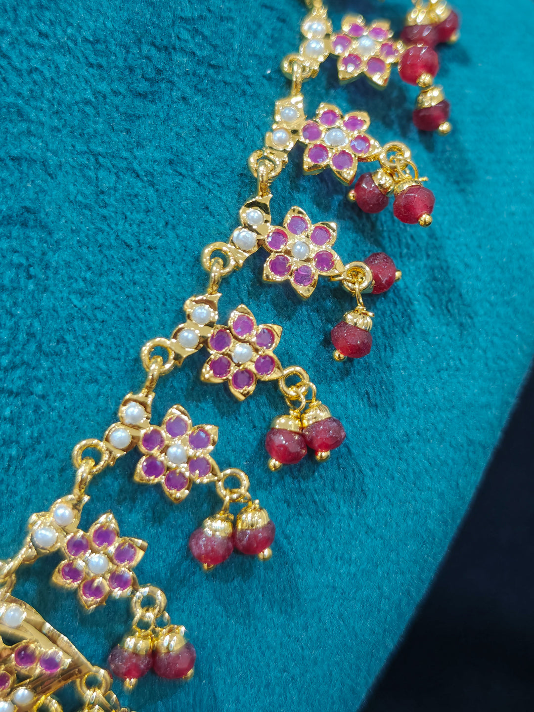 Close-up of a gold Indian traditional jadau jewellery with crystals beads and ruby pink jadau stones. This authentic jadau jewelry set can we worn as jadau necklace set for weddings. Festive celebration look featuring a Jadau artificial necklace.