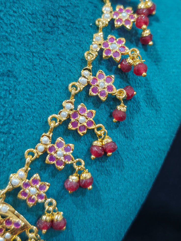 Close-up of a gold Indian traditional jadau jewellery with crystals beads and ruby pink jadau stones. This authentic jadau jewelry set can we worn as jadau necklace set for weddings. Festive celebration look featuring a Jadau artificial necklace.