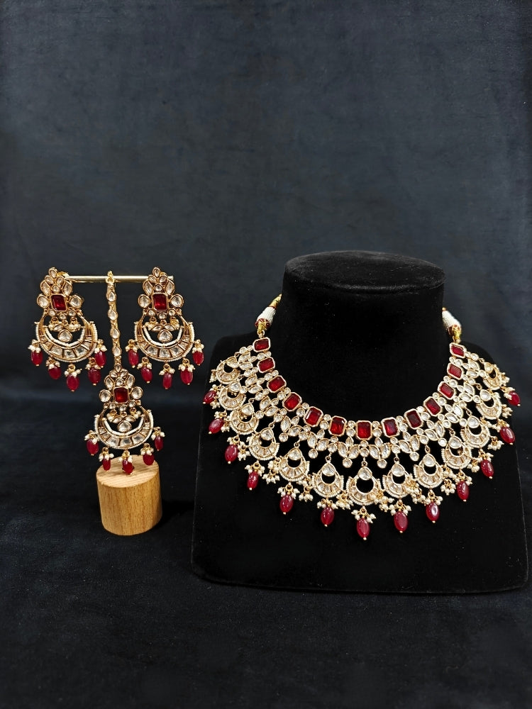 Close-up of an ornate traditional (Gold Polish) Collar jewellery set and earrings and maangtikka with Red Colored Stones, Polki, Kundan, Tumble beads and Pearls. Bride wearing a statement Polki jewelry set for wedding photos. Woman wearing trending Polki artificial jewelry for the wedding season in India.