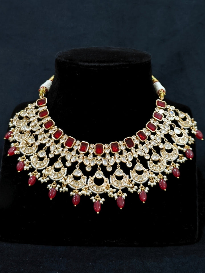 Close-up of an ornate traditional (Gold Polish) Collar jewellery set and earrings and maangtikka with Red Colored Stones, Polki, Kundan, Tumble beads and Pearls. Bride wearing a statement Polki jewelry set for wedding photos. Woman wearing trending Polki artificial jewelry for the wedding season in India.