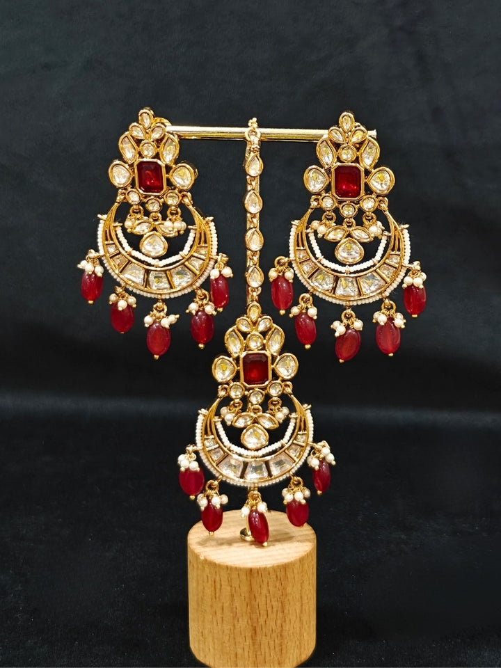 Close-up of an ornate traditional (Gold Polish) Collar jewellery set and earrings and maangtikka with Red Colored Stones, Polki, Kundan, Tumble beads and Pearls. Bride wearing a statement Polki jewelry set for wedding photos. Woman wearing trending Polki artificial jewelry for the wedding season in India.