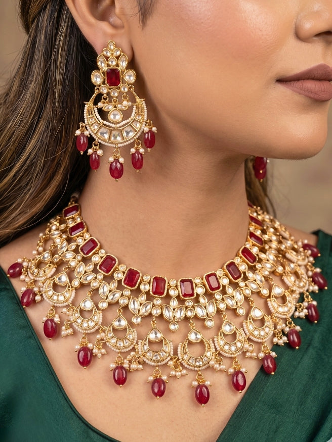 Close-up of a women wearing an ornate traditional (Gold Polish) Collar jewellery set and earrings and maangtikka with Red Colored Stones, Polki, Kundan, Tumble beads and Pearls. Bride wearing a statement Polki jewelry set for wedding photos. Woman wearing trending Polki artificial jewelry for the wedding season in India.