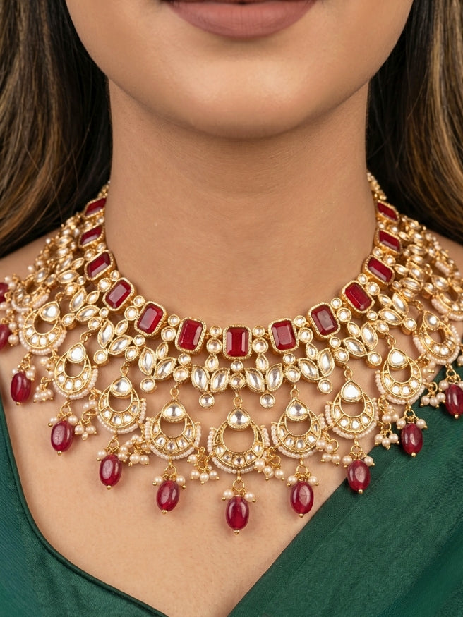 Close-up of a women wearing an ornate traditional (Gold Polish) Collar jewellery set and earrings and maangtikka with Red Colored Stones, Polki, Kundan, Tumble beads and Pearls. Bride wearing a statement Polki jewelry set for wedding photos. Woman wearing trending Polki artificial jewelry for the wedding season in India.