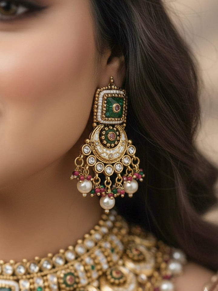 Close-up of a woman wearing an ornate traditional Rajwadi and Heritage gold Choker jewellery set and earrings and maangtikka with Pearls, Beads, Meenakari and Green Colored Stones. Woman pairing a Rajwadi necklace with a red wedding Lehenga. Bride wearing a heritage-inspired artificial necklace set for her wedding ceremony. Close-up of enamel work in Meenakari artificial wedding jewelry.