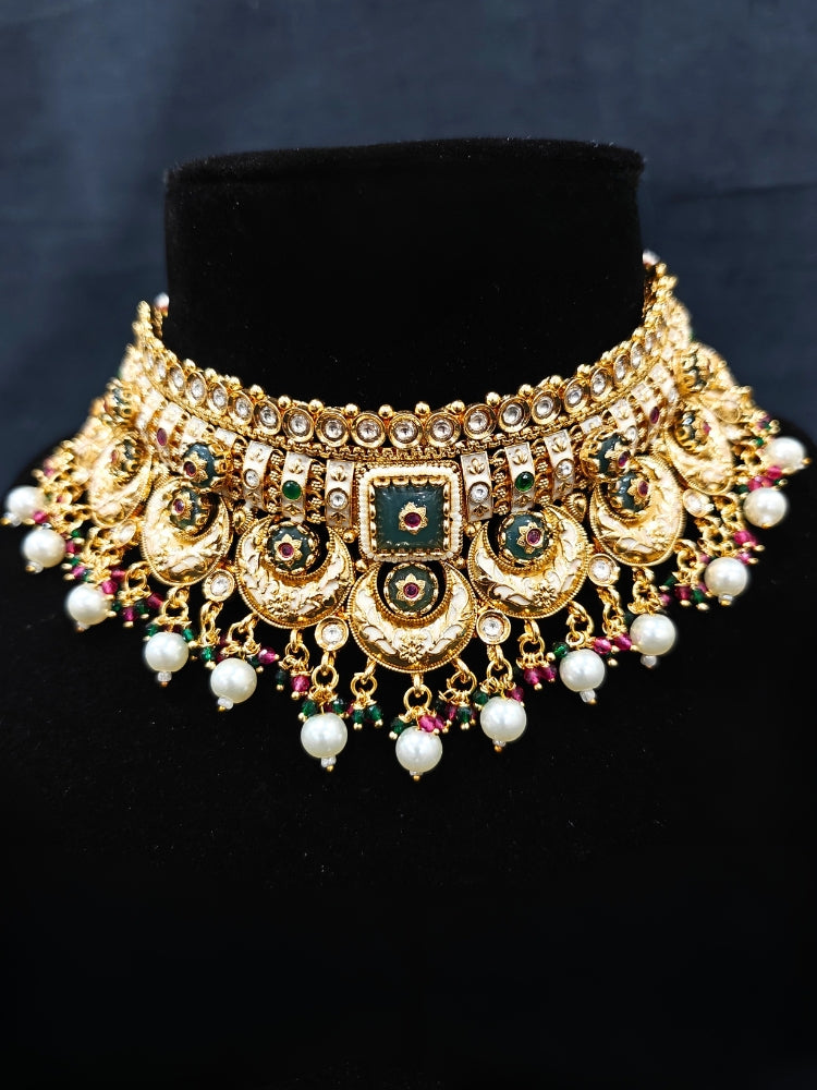 Close-up of an ornate traditional Rajwadi and Heritage gold Choker jewellery set and earrings and maangtikka with Pearls, Beads, Meenakari and Green Colored Stones. Close-up of a premium Rajwadi artificial necklace under 10000. Wedding guest styling a Rajwadi artificial necklace. Luxury wedding styling featuring an antique-inspired artificial Heritage necklace. Close-up of enamel work in Meenakari artificial wedding jewelry.