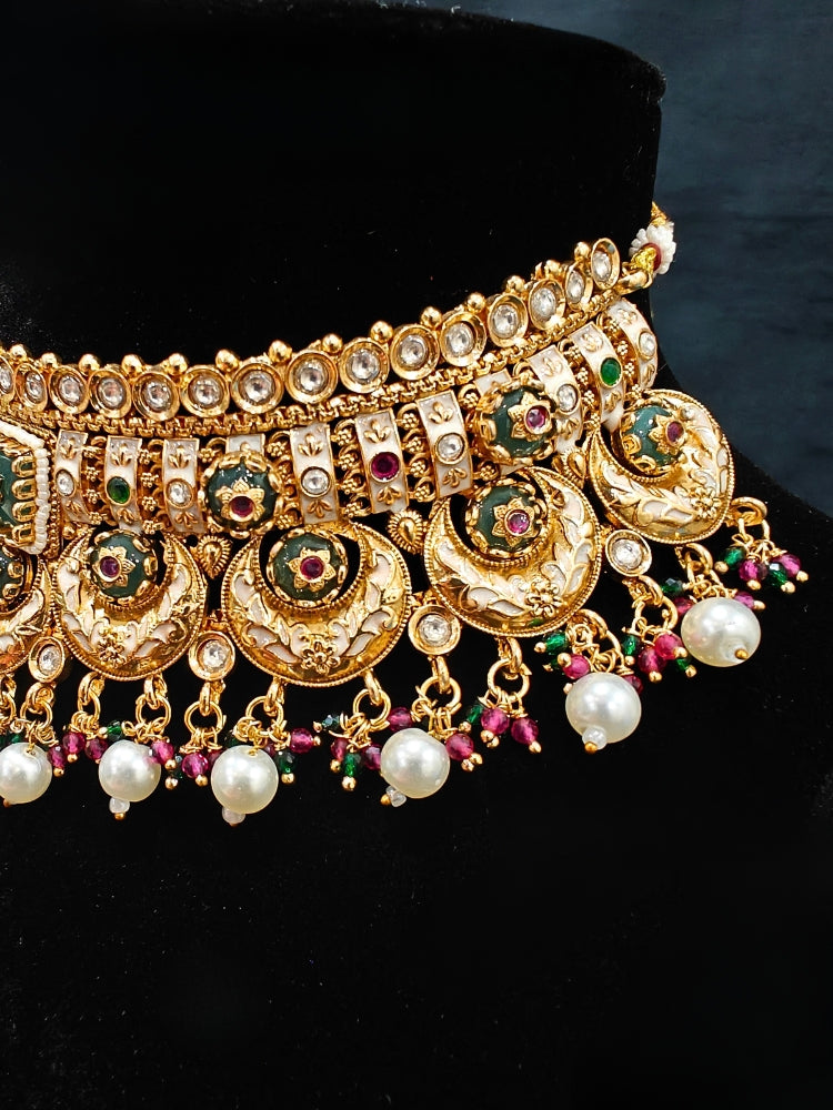 Close-up of an ornate traditional Rajwadi and Heritage gold Choker jewellery set and earrings and maangtikka with Pearls, Beads, Meenakari and Green Colored Stones. Close-up of a premium Rajwadi artificial necklace under 10000. Wedding guest styling a Rajwadi artificial necklace. Luxury wedding styling featuring an antique-inspired artificial Heritage necklace. Close-up of enamel work in Meenakari artificial wedding jewelry.
