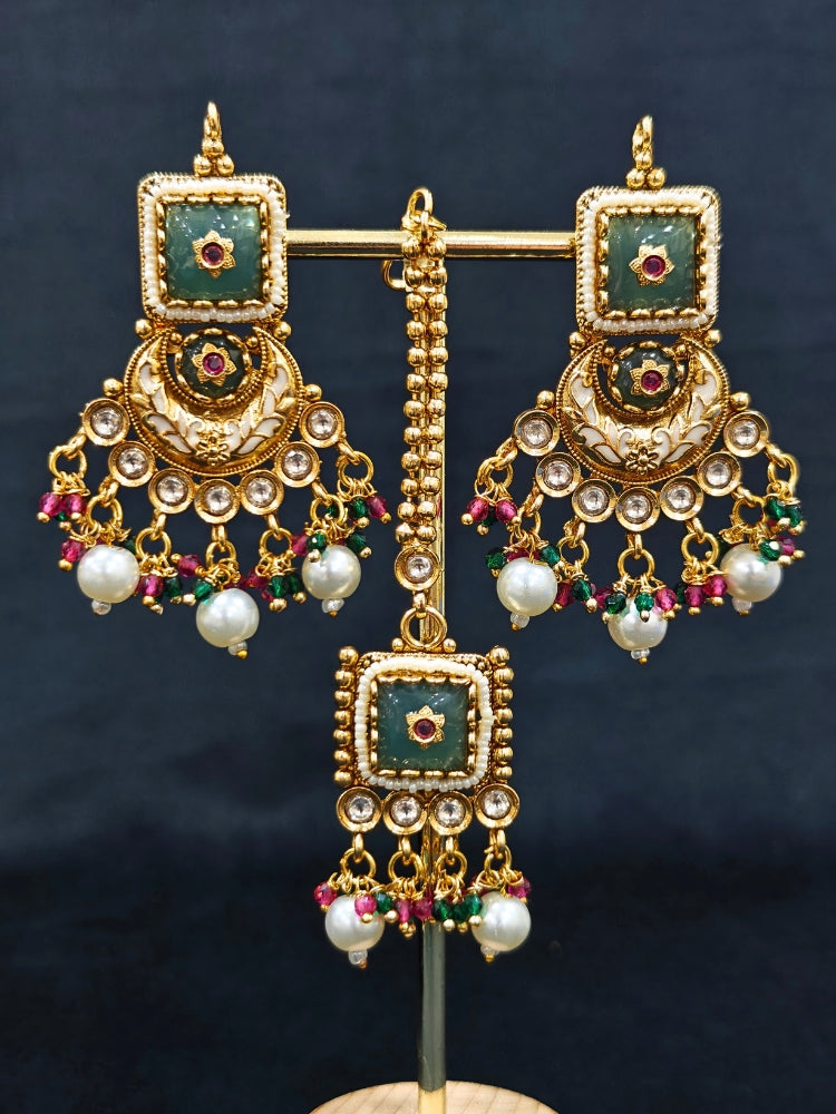 Close-up of an ornate traditional Rajwadi and Heritage gold Choker jewellery set and earrings and maangtikka with Pearls, Beads, Meenakari and Green Colored Stones. Close-up of a premium Rajwadi artificial necklace under 10000. Wedding guest styling a Rajwadi artificial necklace. Luxury wedding styling featuring an antique-inspired artificial Heritage necklace. Close-up of enamel work in Meenakari artificial wedding jewelry.