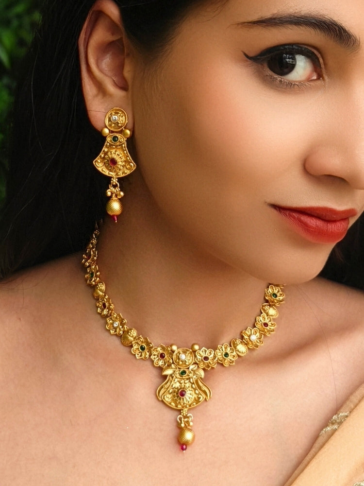 Close-up of a woman wearing an ornate traditional (Gold Polish) Collar jewellery set and earrings with Colored Stones. Mehendi ceremony look completed with a handcrafted Colored Stone jewelry set. Woman wearing trending Colored Stone artificial jewelry for wedding season in India.