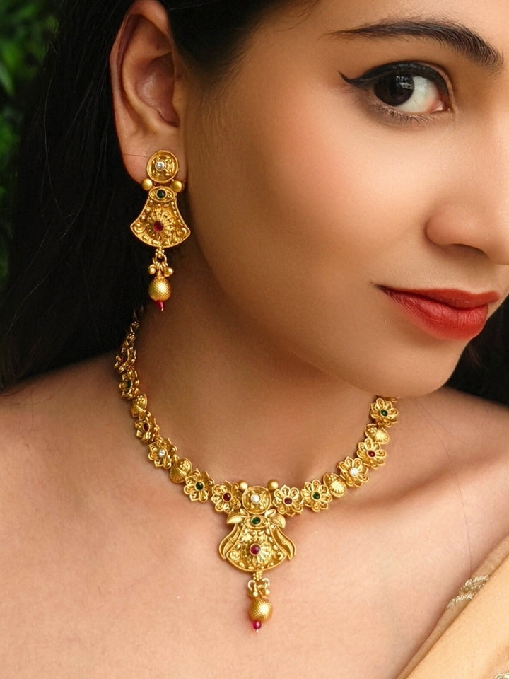 Close-up of a woman wearing an ornate traditional (Gold Polish) Collar jewellery set and earrings with Colored Stones. Mehendi ceremony look completed with a handcrafted Colored Stone jewelry set. Woman wearing trending Colored Stone artificial jewelry for wedding season in India.