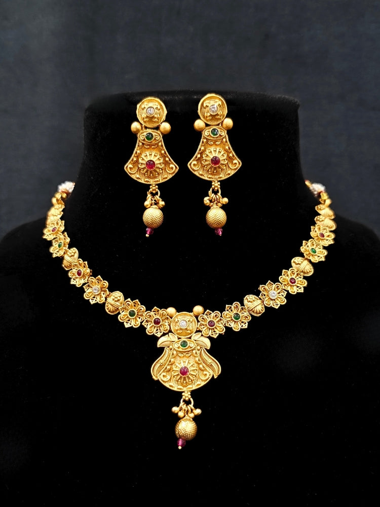 Close-up of an ornate traditional (Gold Polish) Collar jewellery set and earrings with Colored Stones. Mehendi ceremony look completed with a handcrafted Colored Stone jewelry set. Woman wearing trending Colored Stone artificial jewelry for wedding season in India.