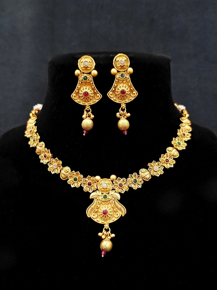 Close-up of an ornate traditional (Gold Polish) Collar jewellery set and earrings with Colored Stones. Mehendi ceremony look completed with a handcrafted Colored Stone jewelry set. Woman wearing trending Colored Stone artificial jewelry for wedding season in India.