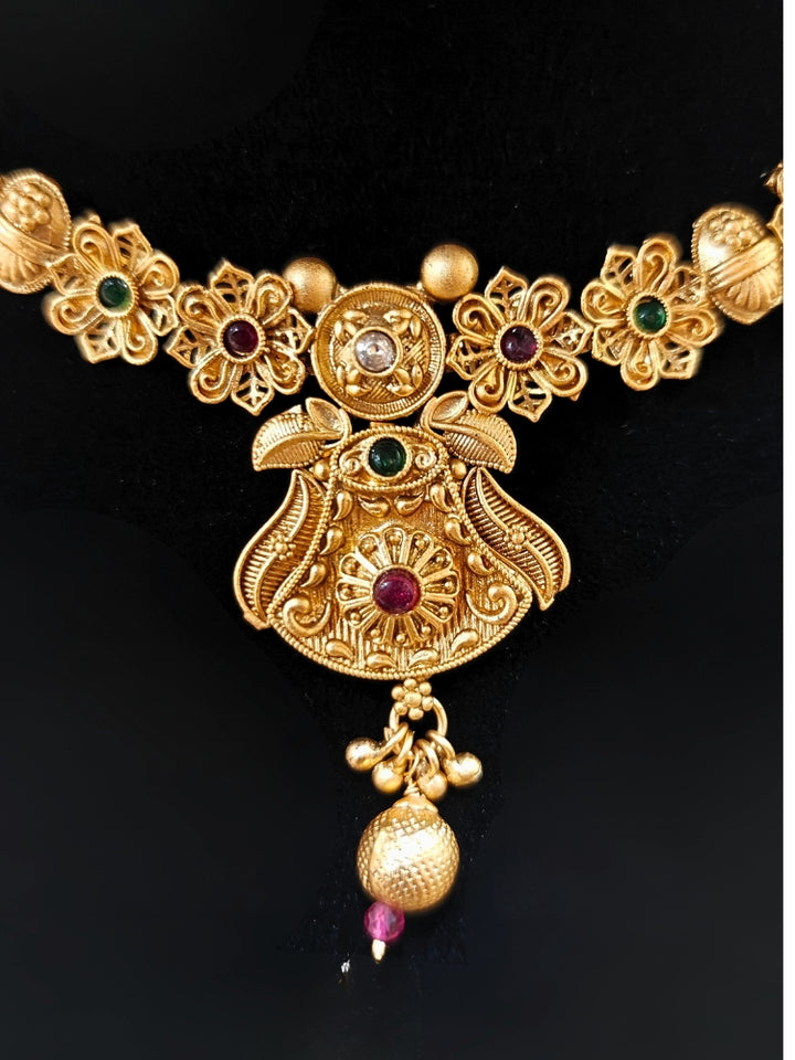 Close-up of an ornate traditional (Gold Polish) Collar jewellery set and earrings with Colored Stones. Mehendi ceremony look completed with a handcrafted Colored Stone jewelry set. Woman wearing trending Colored Stone artificial jewelry for wedding season in India.