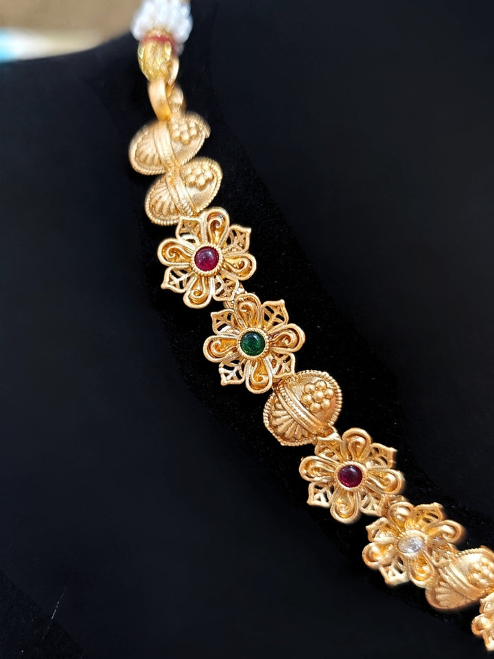 Close-up of an ornate traditional (Gold Polish) Collar jewellery set and earrings with Colored Stones. Mehendi ceremony look completed with a handcrafted Colored Stone jewelry set. Woman wearing trending Colored Stone artificial jewelry for wedding season in India.