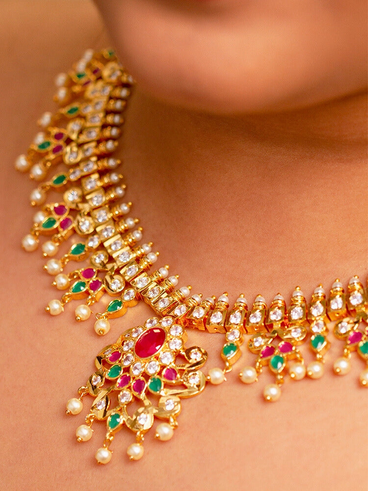 Close-up of a woman wearing an ornate traditional (Gold Polish) Collar jewellery set and earrings with pearls, ruby &amp; Emerald Colored Stone and American Diamond. Festive Diwali outfit styled with an American diamond artificial necklace. Close-up shot of a high-quality American diamond artificial necklace worn for festive celebrations.
