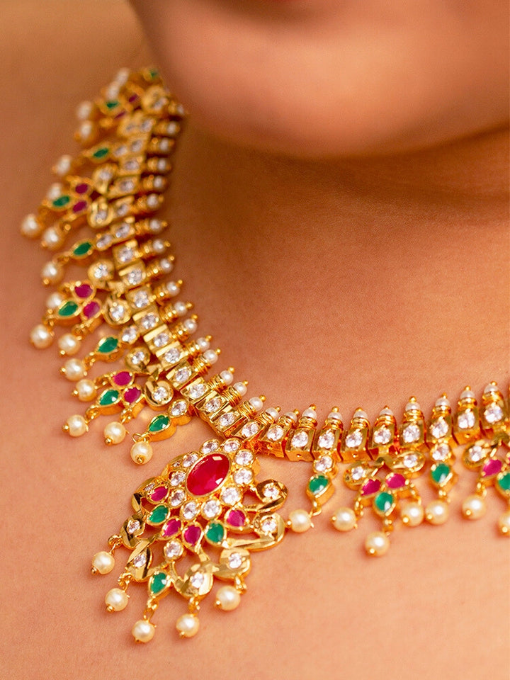 Close-up of a woman wearing an ornate traditional (Gold Polish) Collar jewellery set and earrings with pearls, ruby &amp; Emerald Colored Stone and American Diamond. Festive Diwali outfit styled with an American diamond artificial necklace. Close-up shot of a high-quality American diamond artificial necklace worn for festive celebrations.